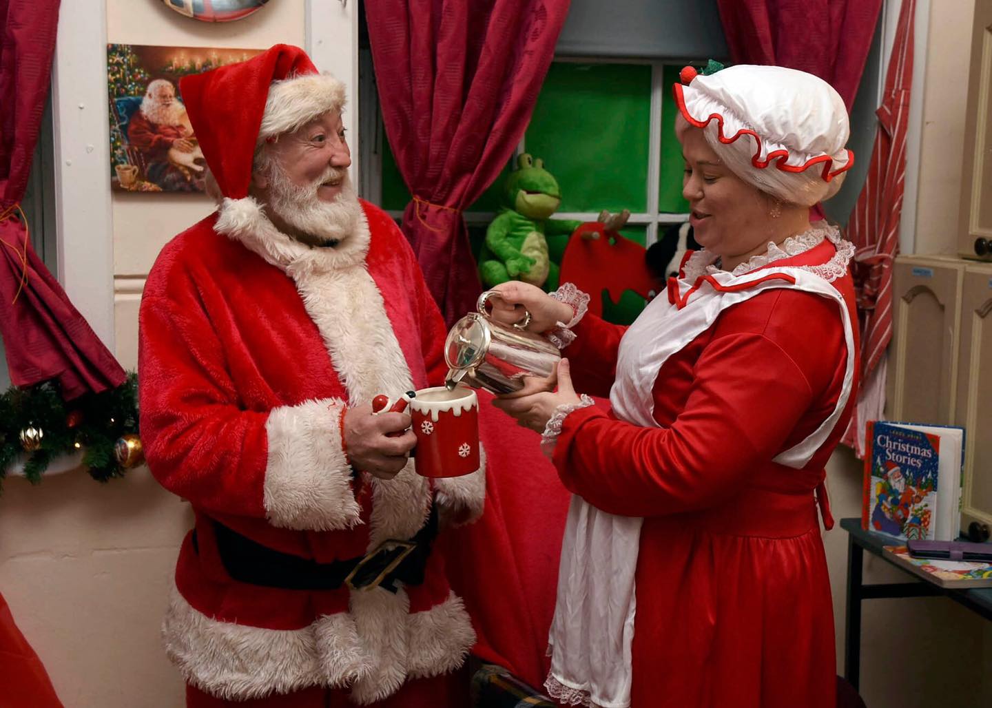 Mrs Claus pouring tea from a silver teapot for Santa in Christmas room-set